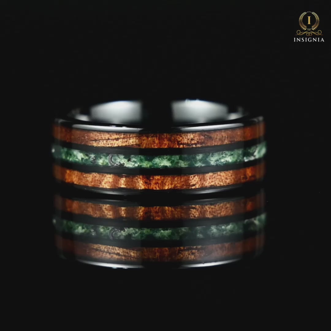 A video of a dark men's wedding band with moss agate rotating on a reflective black glass surface, highlighting its design.