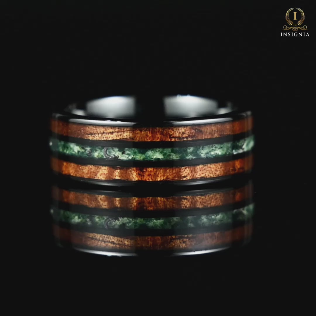 A video of a dark men's wedding band with moss agate rotating on a reflective black glass surface, highlighting its design.